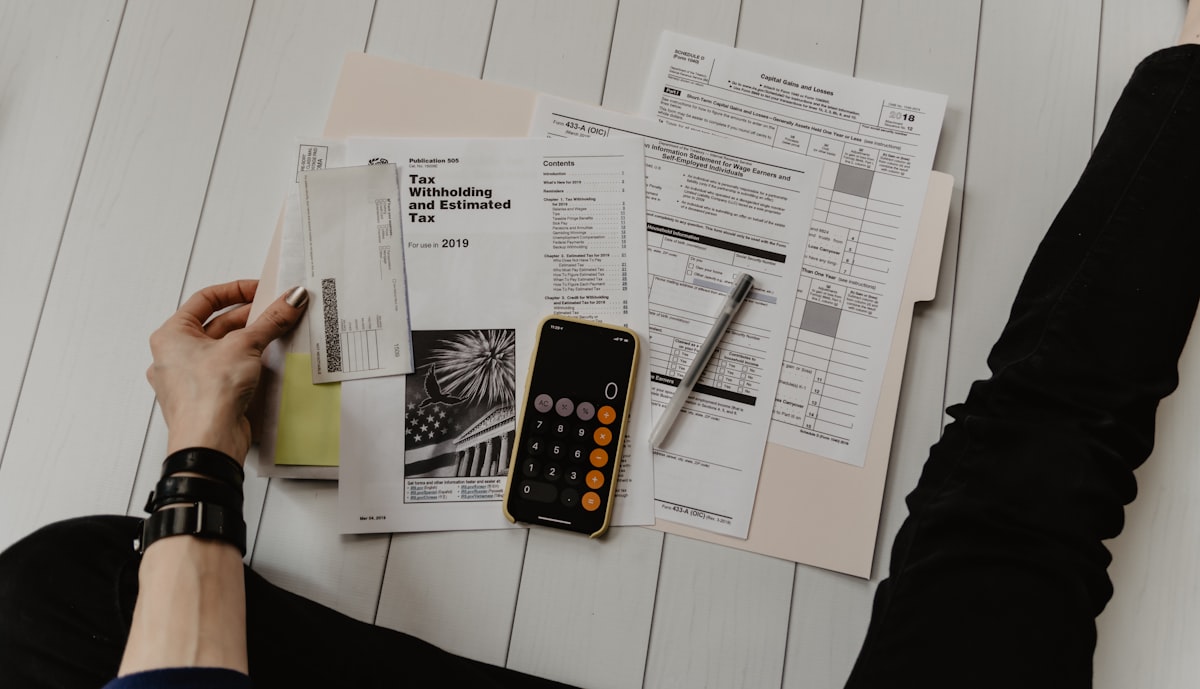 Overhead view of tax documents including a 2019 Tax Withholding form, a calculator, and a pen on a light desk.